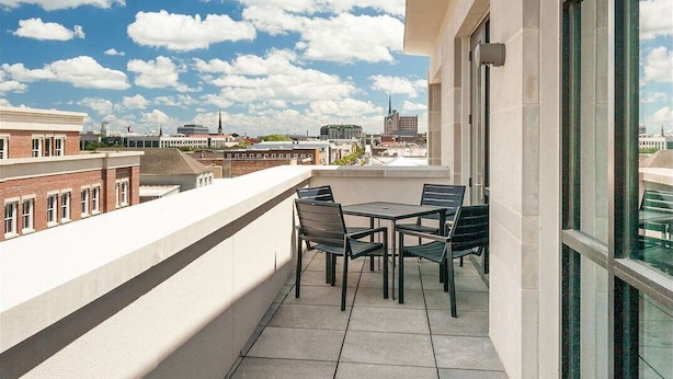 Un balcón con mesa y sillas, con vista a un paisaje urbano de edificios y cielo despejado.