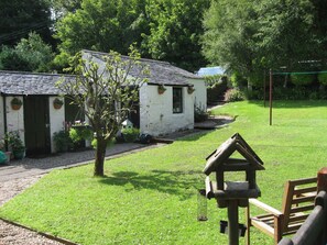 Ein rustikales weißes Cottage mit Ziegeldach, umgeben von üppigem Grün und einem gepflegten Rasen.