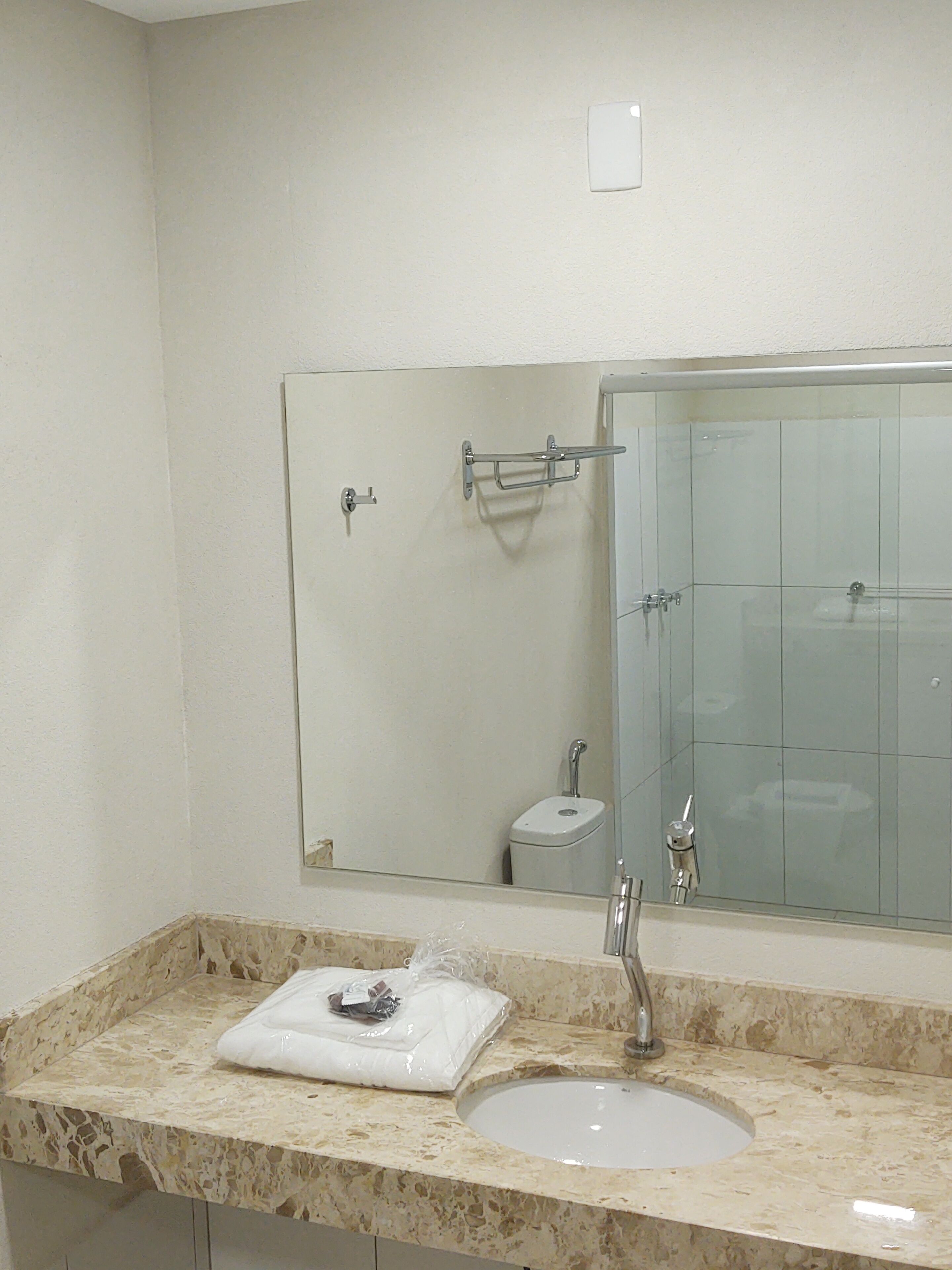 Un baño con lavamanos de mármol, un espejo, una toalla y cabina de ducha de vidrio.