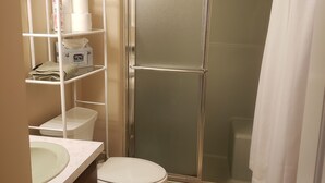 A bathroom with a toilet, a sink, a shower with a glass door, and a shelf with toiletries. - Private 4 BR Ranch Tucked In The Woods 1.5 Miles From Beach (Falmouth)