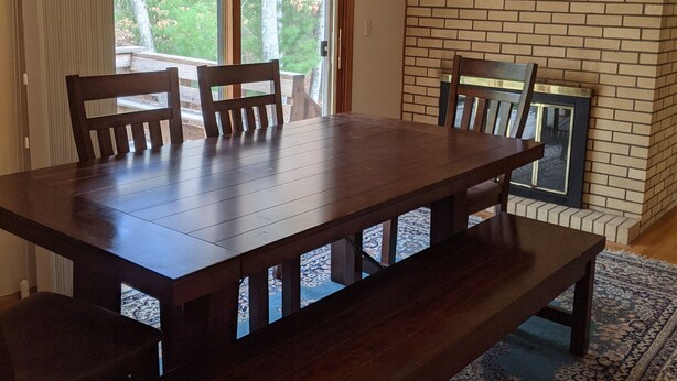 A dining area with a large wooden table, chairs, a hanging light fixture, and a brick fireplace. - Private 4 BR Ranch Tucked In The Woods 1.5 Miles From Beach (Falmouth)