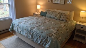 A bedroom with a floral bedspread, two bedside lamps, and three wall-mounted pictures. - Private 4 BR Ranch Tucked In The Woods 1.5 Miles From Beach (Falmouth)