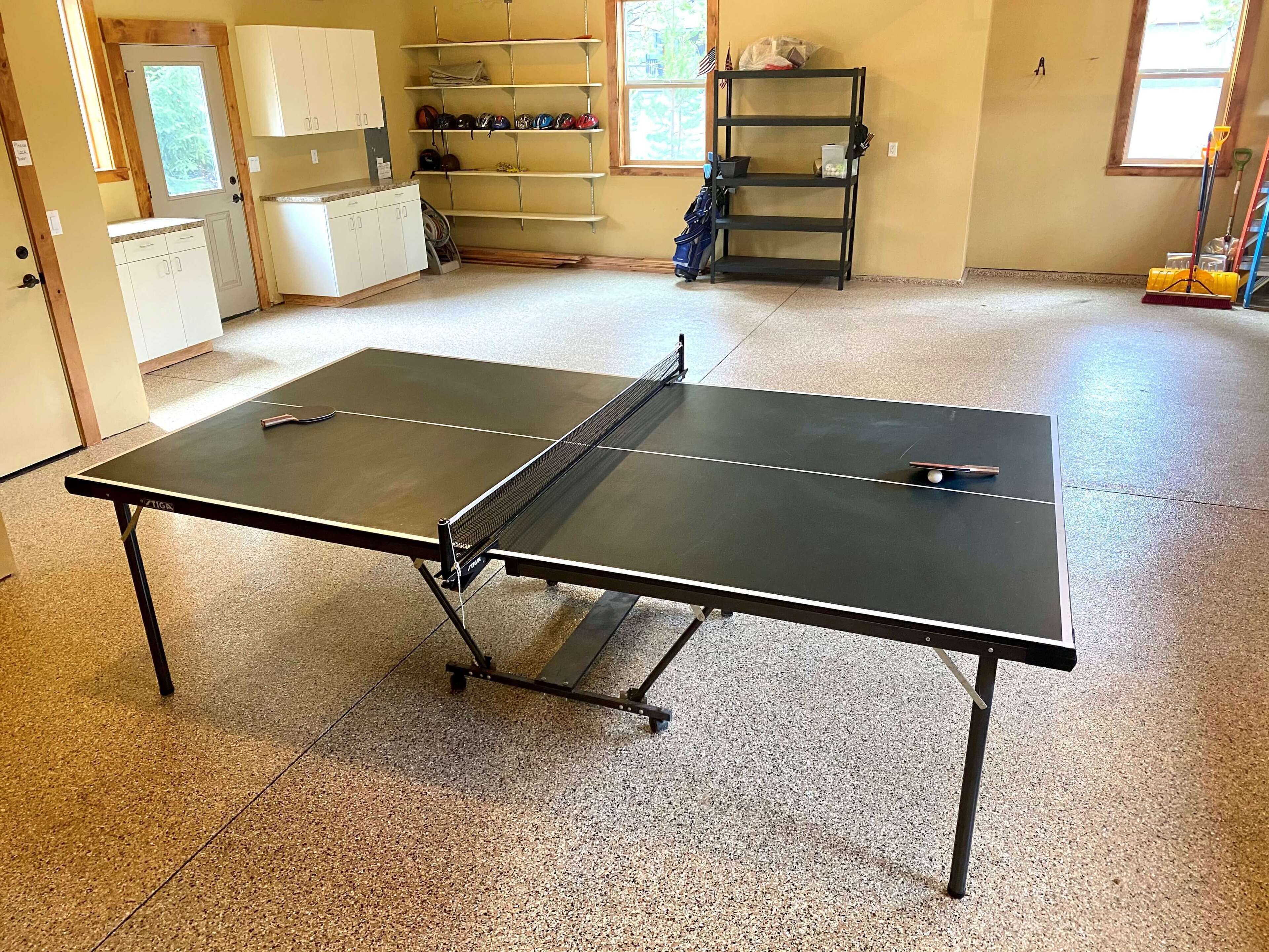 Une table de ping-pong dans une pièce équipée d’un coin cuisine, d’étagères et d’une fenêtre.