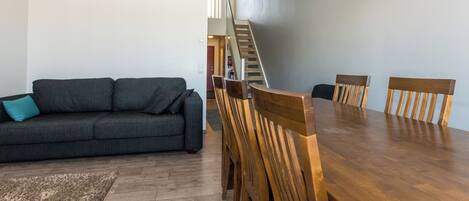 Een woonkamer met een bank, een eettafel met stoelen en een trap naar een hoger gelegen verdieping.