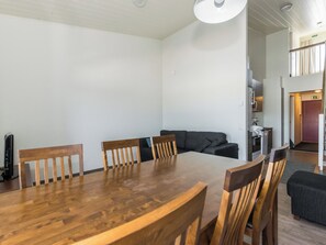A dining area with a wooden table and chairs, a sofa, and a kitchen in the background.