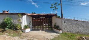 A gated entrance with a metal gate, a white wall, and a tiled roof. - Chácara Recanto dos Pássaros 2 (SP)