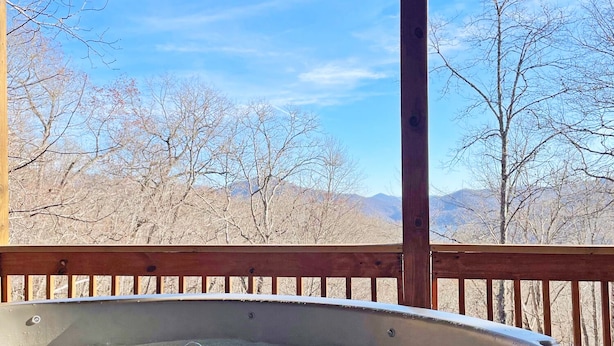 Ein Whirlpool unter einer Holzterrasse mit Blick auf kahle Bäume und Berge im Hintergrund.