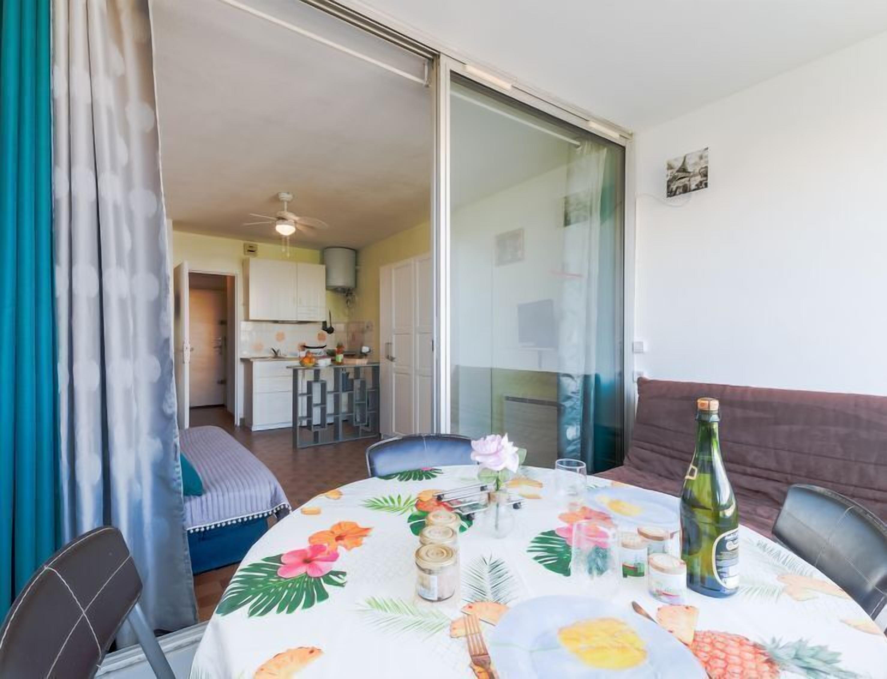Una mesa de comedor dispuesta con mantel de temática tropical, una botella de vino y diferentes condimentos.