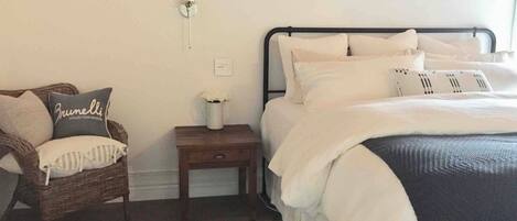 A bedroom with a bed, a nightstand, a wicker chair, and a wall-mounted light fixture.