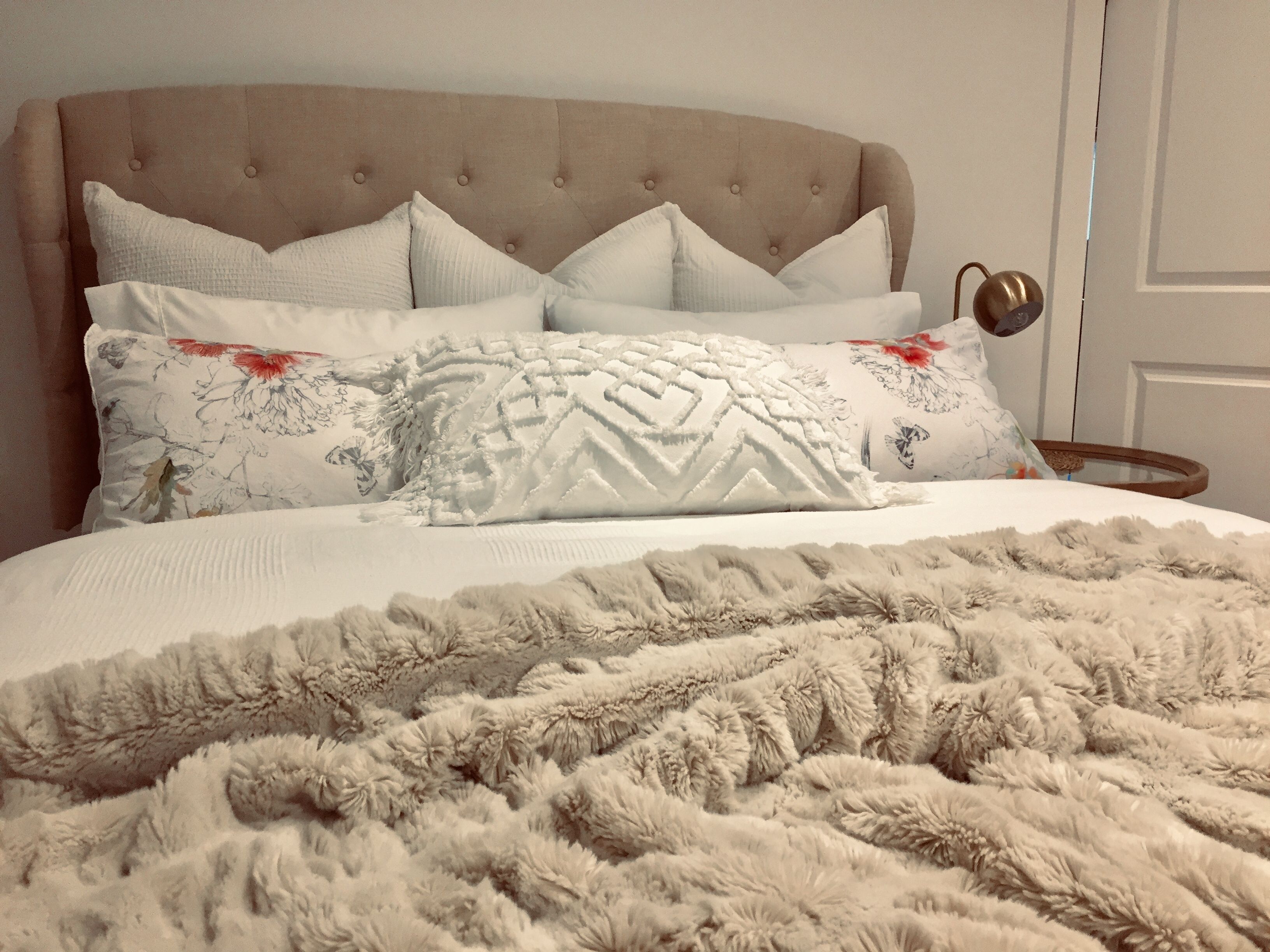 A bed with a tufted headboard, multiple pillows, and a fluffy blanket.