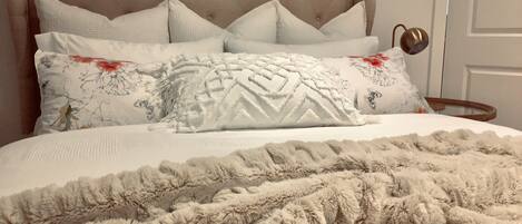 A bed with a tufted headboard, multiple pillows, and a fluffy blanket.