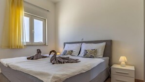 A neatly made bed with a white duvet, a grey headboard, and two bedside tables with lamps. - Apartment Rok 2 by Interhome (Pula/Banjole)