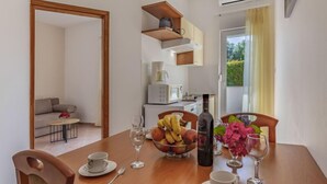 A dining area with a wooden table set for two, a bowl of fruit, a bottle of wine, and a vase of flowers. - Apartment Rok 2 by Interhome (Pula/Banjole)