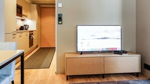 A modern living room with a flat-screen TV on a wooden cabinet, a kitchen area with cabinets and a coffee maker, and a wooden door leading to another room. - Levin kunkku b5 by Interhome (Kittilä)
