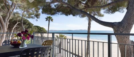 A balcony with a table and chairs, overlooking a beach and the sea.