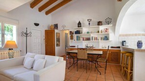 A spacious living area with a white sofa, a dining table with chairs, and a kitchen area with shelves and a bar. - Flamenco by Interhome (Calpe/Calp)