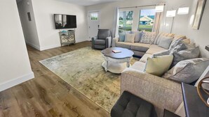 A living room with a sofa, armchairs, a coffee table, a TV, and a large window with curtains.