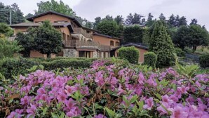 Un edificio de varios pisos con fachada de piedra, rodeado de exuberante vegetación y plantas en flor.