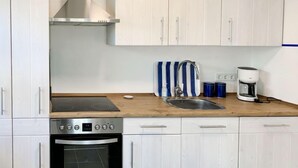 Une cuisine moderne avec des meubles blancs, un four encastré, une plaque de cuisson, un évier et une machine à café.
