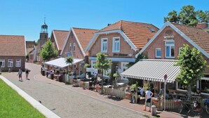 Une rue bordée de bâtiments traditionnels en briques, dont certains arborent des enseignes bien visibles, sous un ciel bleu dégagé.