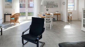 Un salon moderne avec un fauteuil noir, une table à manger blanche et une vue sur l’extérieur.