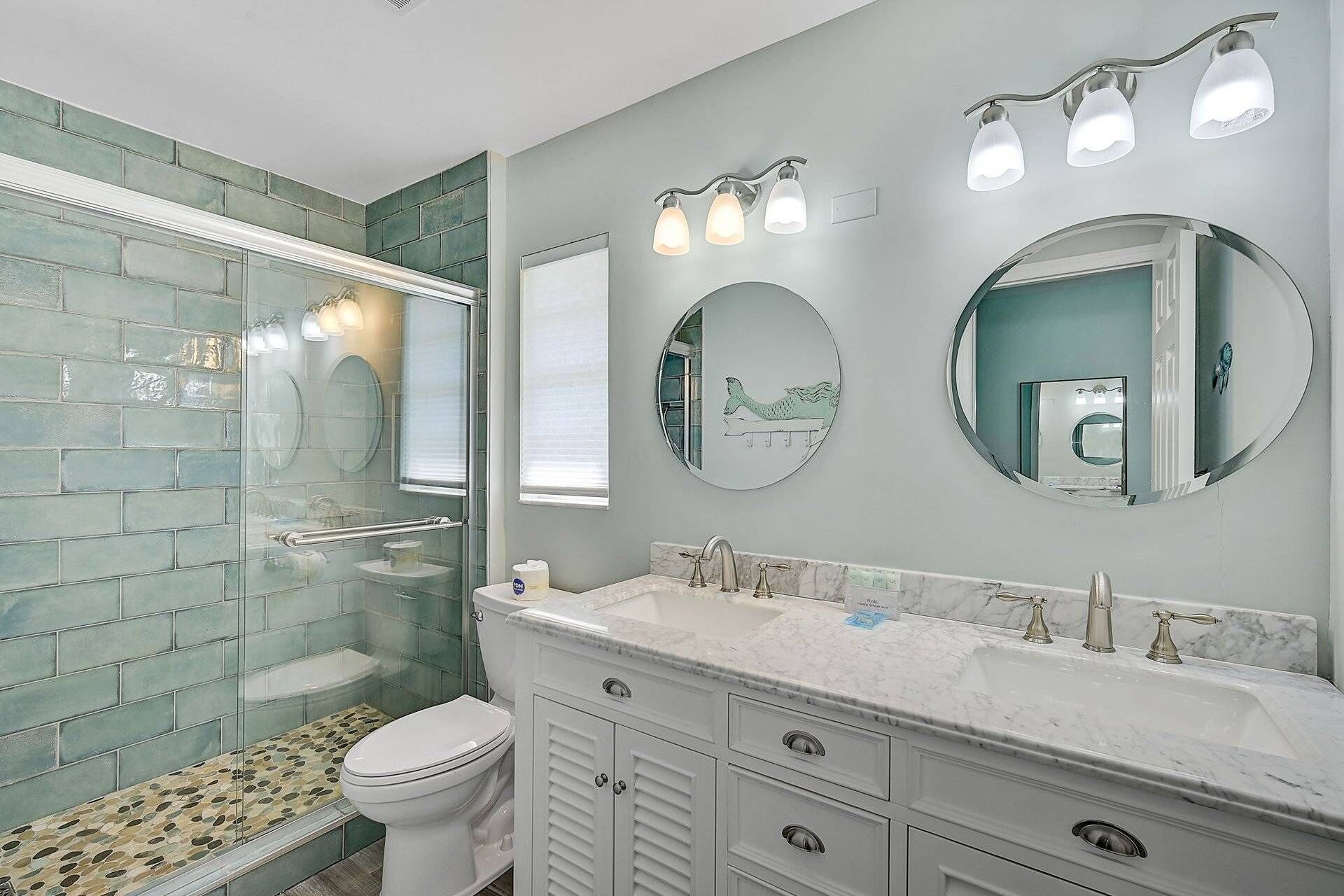 A bathroom with a glass shower enclosure, a white toilet, a marble sink with a vanity, and two wall-mounted mirrors.