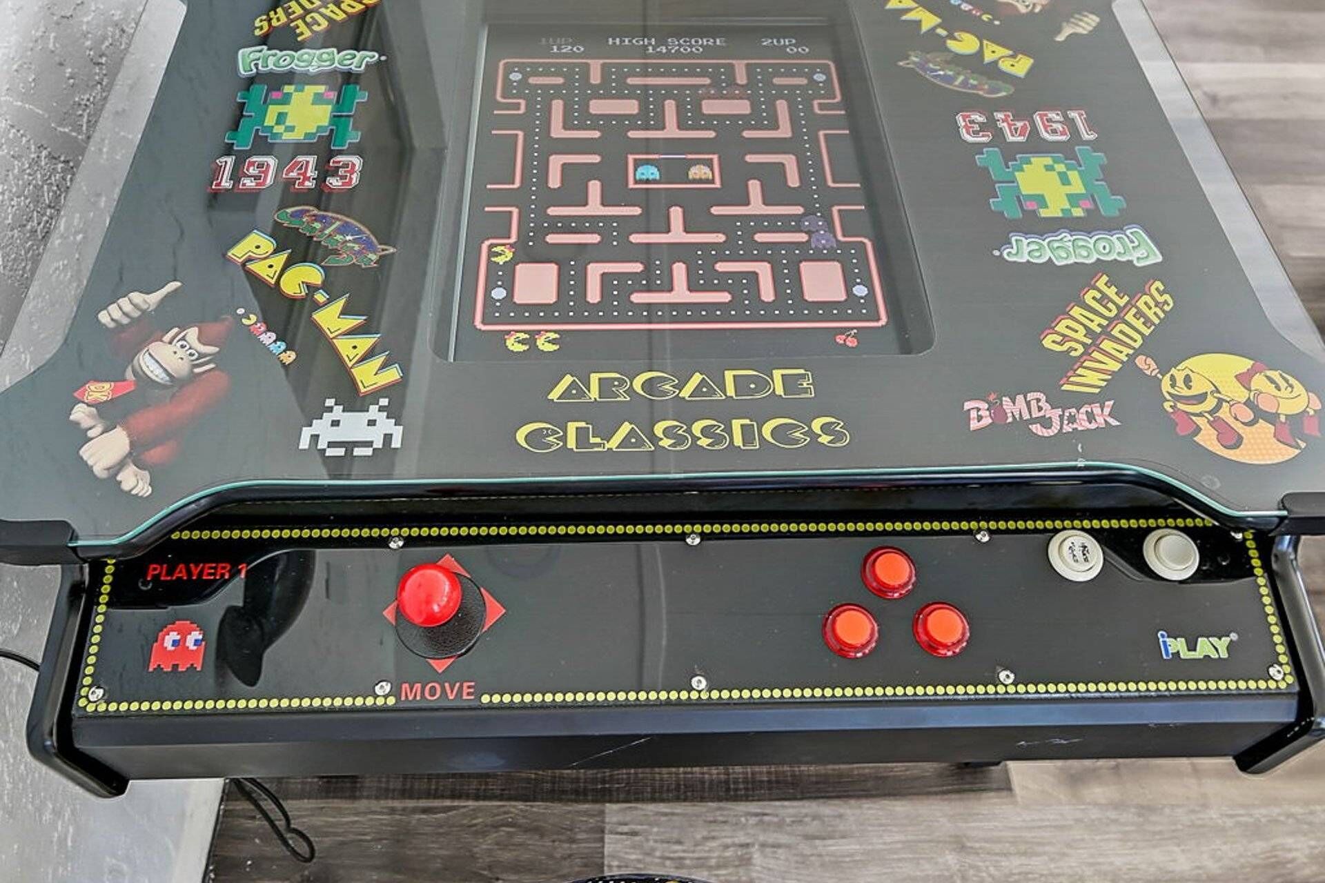 A retro arcade table with classic games like Space Invaders and Pac-Man, featuring a joystick and buttons for gameplay.