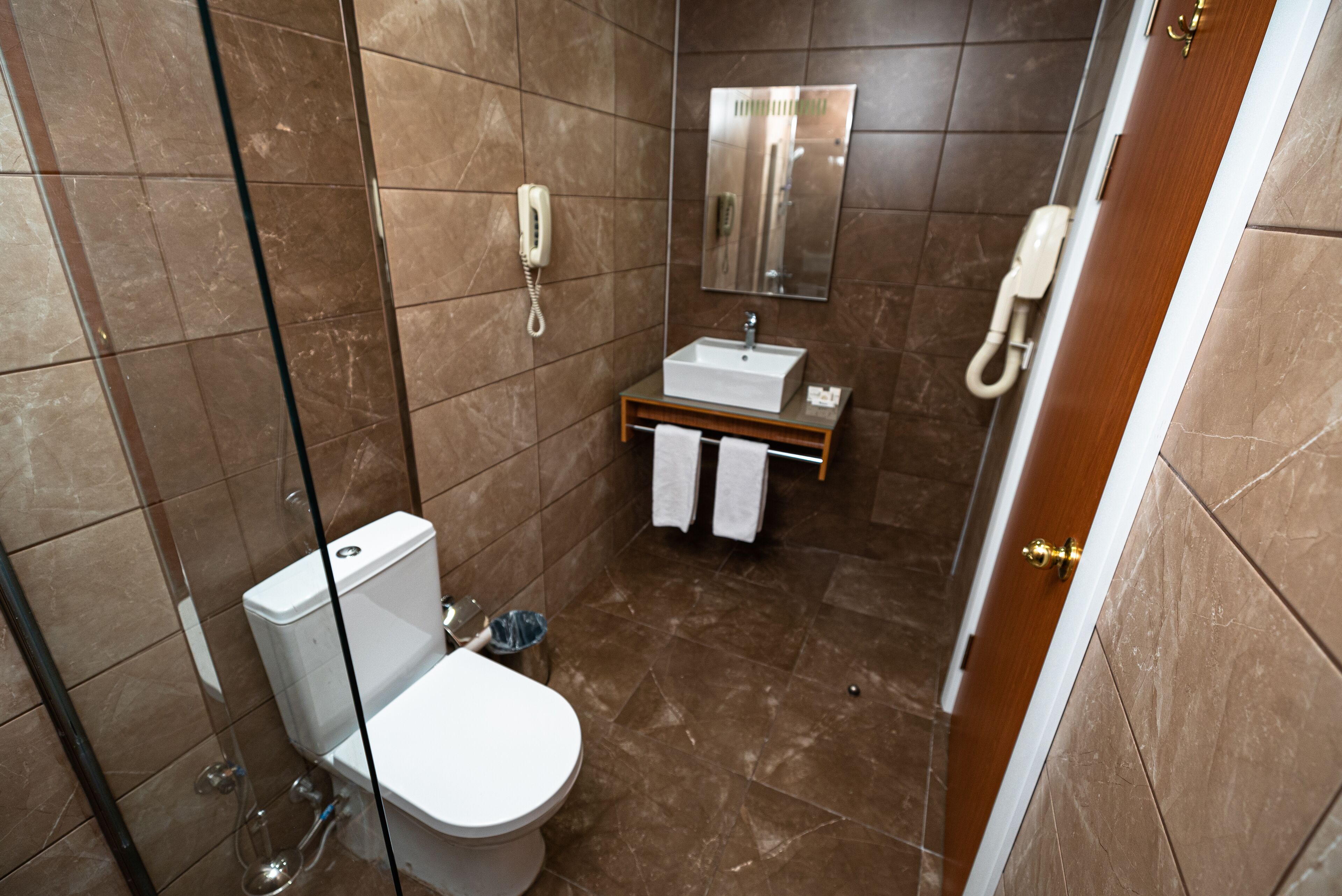 Un baño moderno con inodoro, lavamanos y dos teléfonos instalados en la pared.