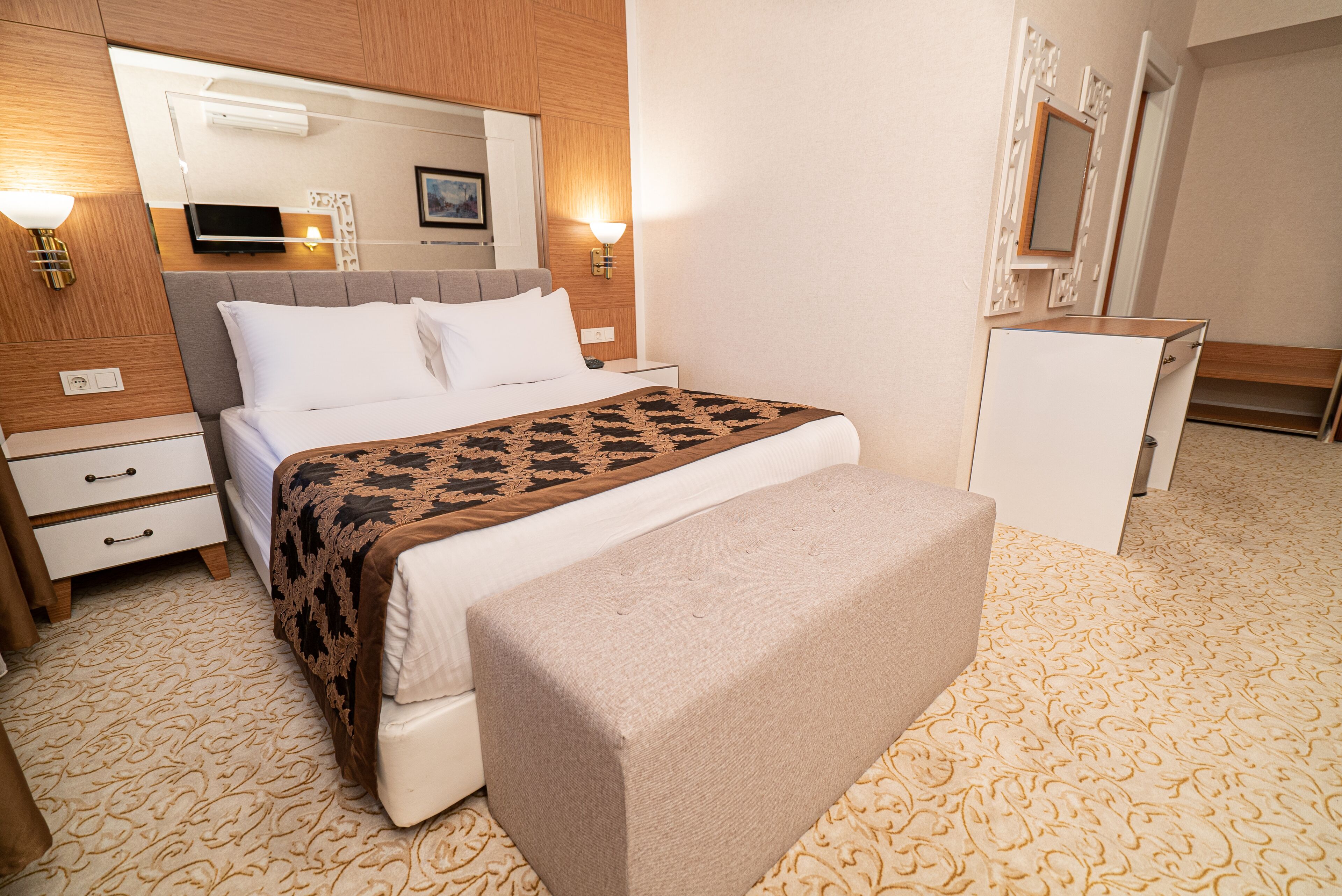 A hotel room with a bed, bedside tables, a bench, a TV, and a mirror.