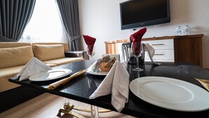 Habitación de hotel con comedor que incluye una mesa negra, platos blancos, servilletas rojas y un televisor de pantalla plana montado en la pared.