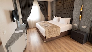 Una habitación de hotel moderna con una cama grande, una mesita de noche, un televisor montado en la pared y suelo de madera.