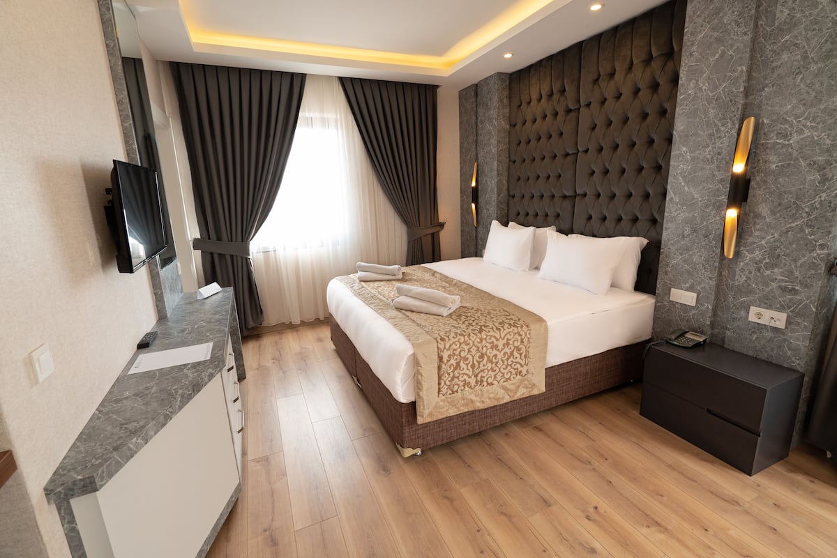 A modern hotel room with a large bed, a bedside table, a TV mounted on the wall, and a wooden floor.