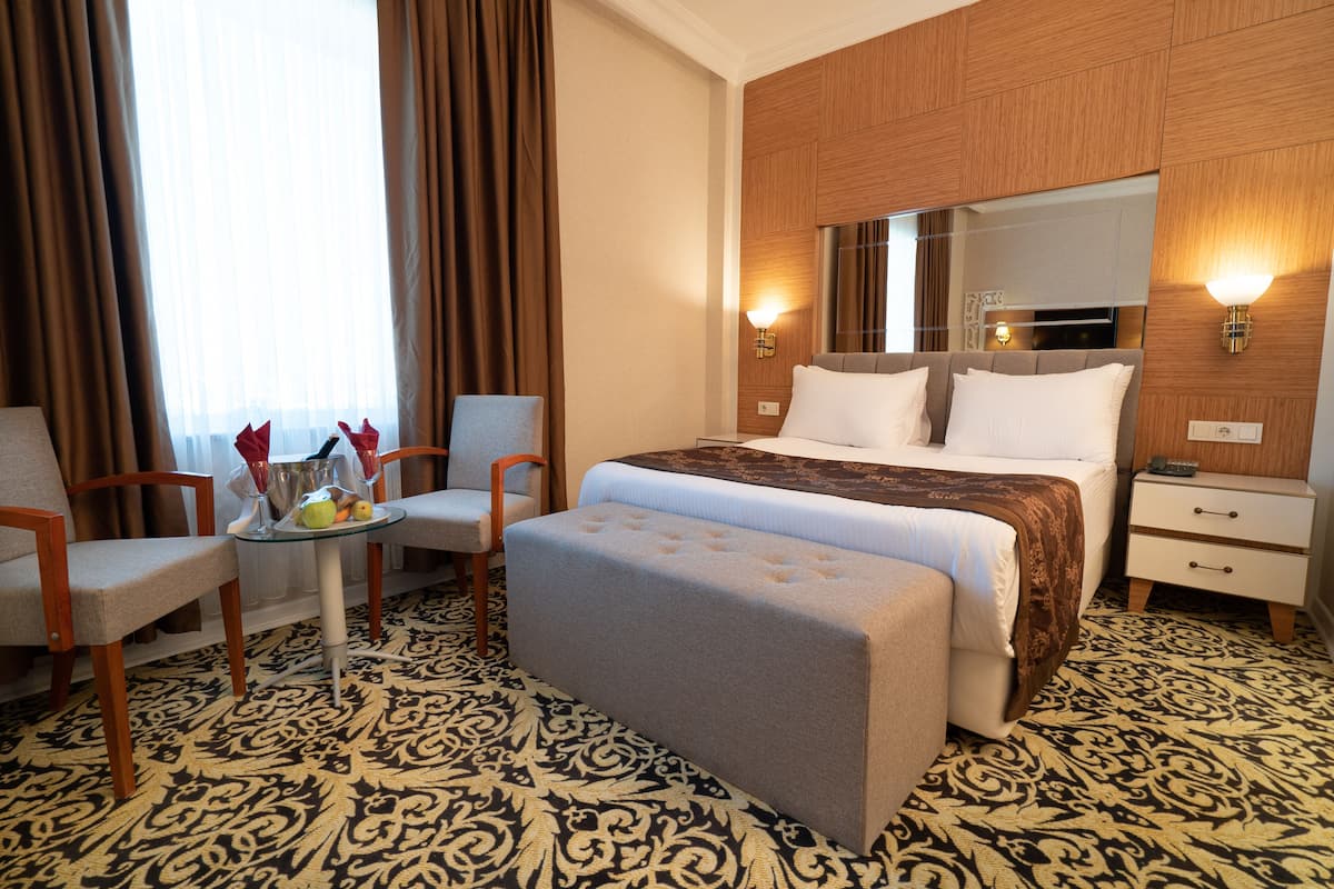 A hotel room with a large bed, a sitting area with a table and chairs, a nightstand, and a mirror above the bed.
