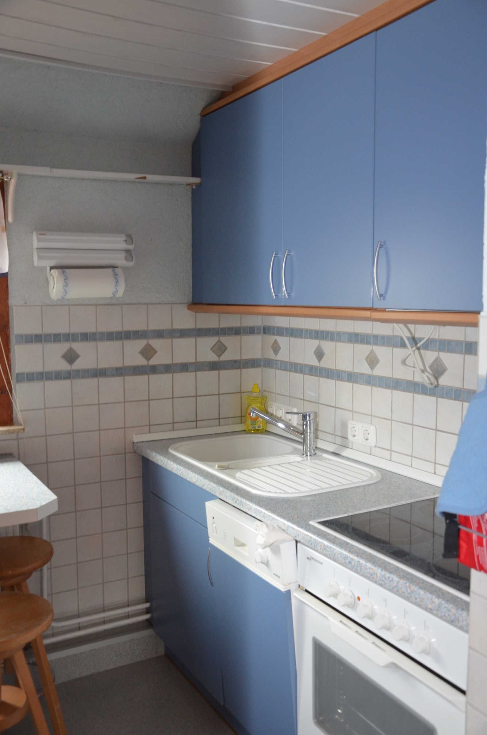 Una cocina con armarios azules, un lavamanos blanco y una estufa.