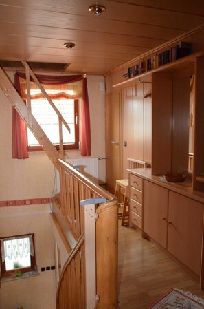 A wooden staircase leading to an upper floor, a kitchen area with wooden cabinets, and a window with curtains. - Ferienwohnung Westphal (Eschwege)