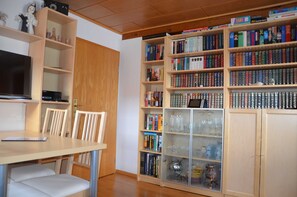 Ein Zimmer mit Holztisch, Stühlen, einem Fernseher und einem Bücherregal, das mit Büchern und Dekoration gefüllt ist.