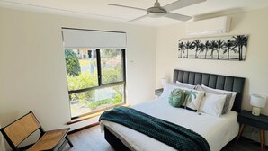A bedroom with a bed, a ceiling fan, a window with a view, and a chair.