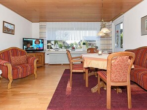 A living room with a television, a dining table with chairs, and a sofa.