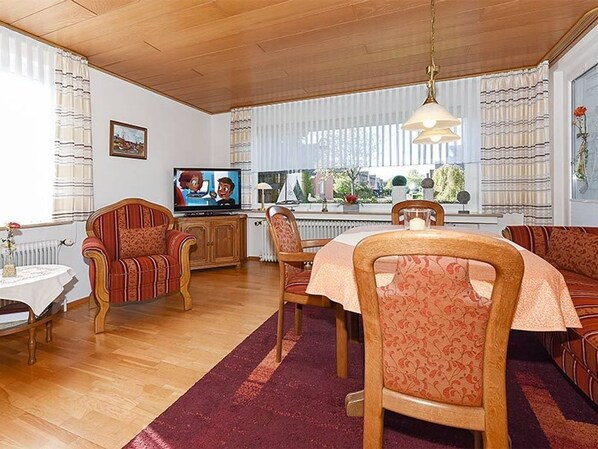 Un comedor con una mesa, sillas, un televisor y una ventana con cortinas.