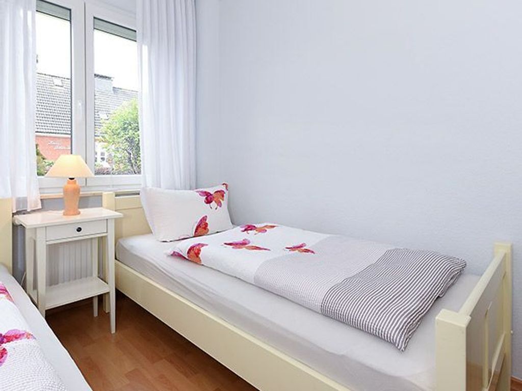 Un lit simple avec un coussin à motifs floraux, une table de chevet avec une lampe et une fenêtre avec des rideaux.