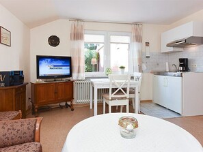 A compact living space with a dining area, kitchenette, and a television displaying 'Nachrichten'.