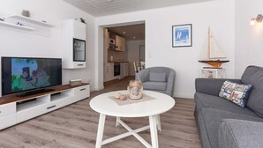 A living room with a TV, a round white coffee table, a grey sofa, and a grey armchair. - Ferienwohnung 6 - Haus Windliese (Esens)