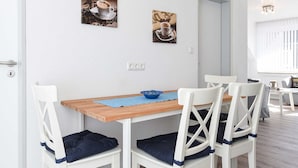 A dining area with a wooden table and white chairs, a blue placemat, and two wall-mounted pictures. - Ferienwohnung 6 - Haus Windliese (Esens)