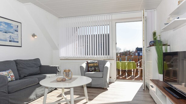 A modern living room with a grey sofa, a white coffee table, a grey armchair, and a TV on a wooden cabinet. - Ferienwohnung 6 - Haus Windliese (Esens)