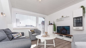 A modern living room with a grey sofa, a round white coffee table, and a flat-screen TV on a white cabinet. - Ferienwohnung 6 - Haus Windliese (Esens)