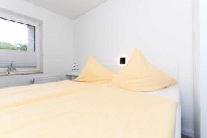 Ein Schlafzimmer mit einem Bett, einem Fenster, einer Heizung und einem Nachttisch mit einer Lampe.