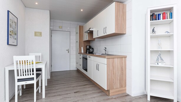 Une cuisine compacte avec des meubles blancs, un plan de travail en bois et un petit coin repas comprenant une table et une chaise, le tout dans des tons blancs.