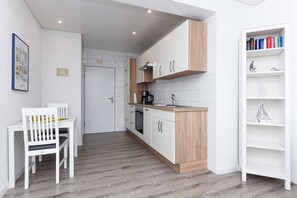 Eine kleine Küche mit weißen Schränken, einer Holz Arbeitsplatte und einem Essbereich mit einem weißen Tisch und einem Stuhl.
