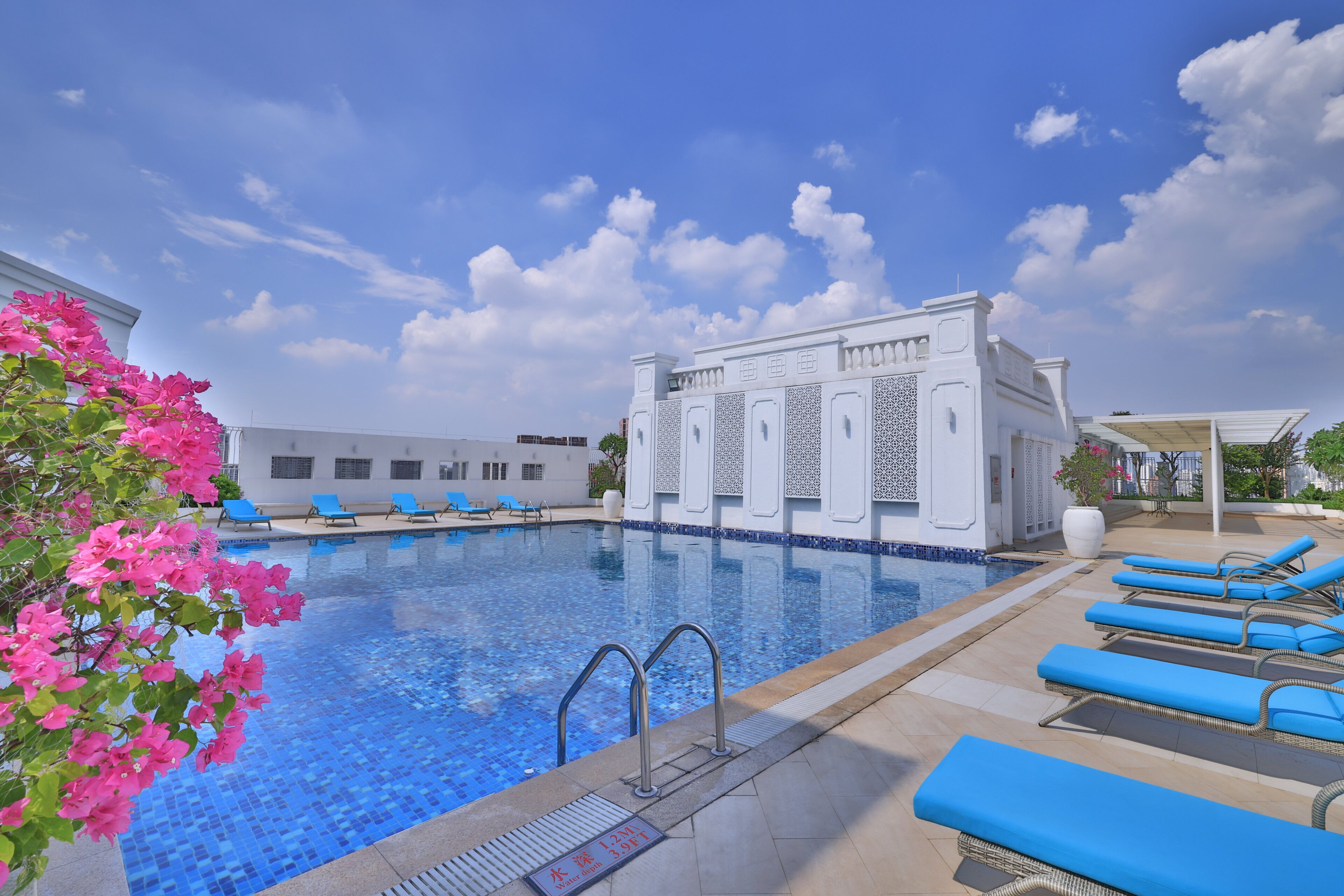 Una piscina con azulejos azules, rodeada de sillas de descanso y un edificio blanco de diseños intrincados.