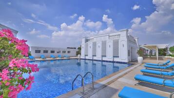Una piscina con azulejos azules, rodeada de sillas de descanso y un edificio blanco de diseños intrincados.